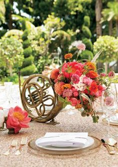 an arrangement of flowers and music instruments sits on a table set for a formal dinner