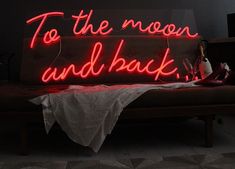 a neon sign that says to the moon and back on a couch in a dark room