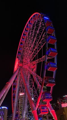 a ferris wheel lit up at night with buildings in the background