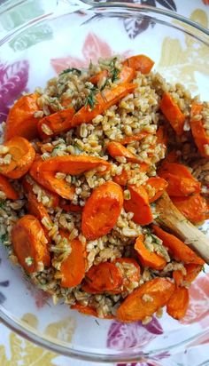 a bowl filled with rice and carrots on top of a floral table cloth next to a wooden spoon