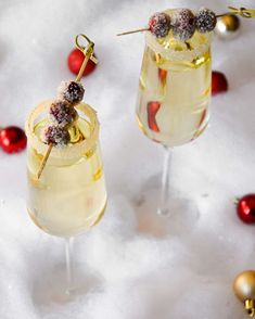 two glasses filled with champagne sitting on top of snow next to red and gold ornaments