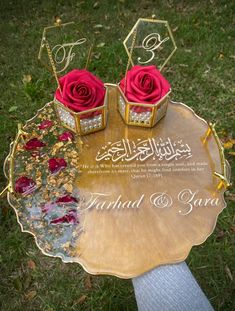 two red roses sitting on top of a gold plate with the names of each couple