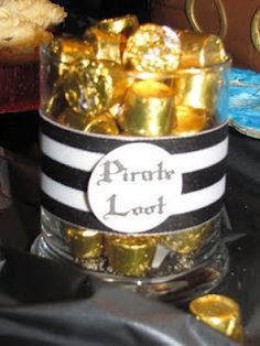 a glass container filled with lots of gold foil wrapped in black and white ribbon on top of a table