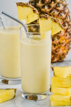 two glasses filled with pineapple milk next to sliced pineapples