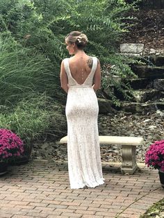 a woman in a white dress is looking at some plants and flowers on the ground