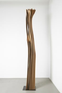 a tall wooden sculpture sitting on top of a cement floor next to a white wall