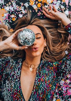 a woman holding a disco ball up to her face while laying on the ground with confetti all around her