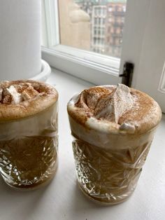 two cups filled with hot chocolate sitting on top of a counter next to a window