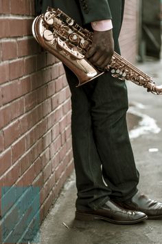 a man is holding a saxophone leaning against a brick wall