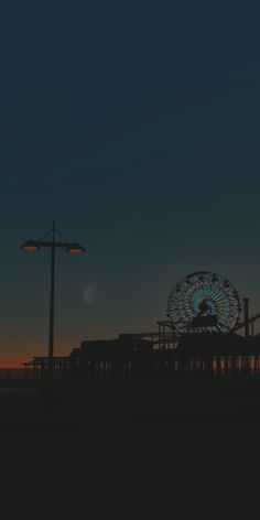 a ferris wheel sitting on top of a pier next to a tall light pole at night