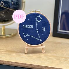 a cross - stitch zodiac sign on a wooden stand next to a clock with the word pisces printed on it