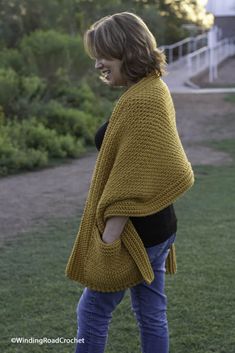 a woman standing in the grass wearing a yellow knitted ponchy shawl