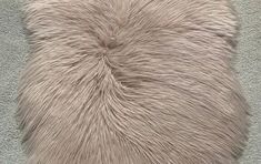 the back side of a sheepskin pillow on a gray carpeted floor with white fur