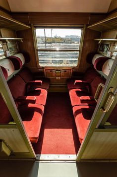 the inside of a train car with red seats and windows looking out onto the tracks