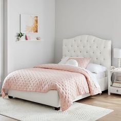 a white bed with pink comforter and pillows in a light colored room next to a window