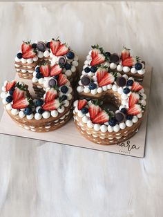 two cakes decorated with strawberries and blueberries are on a wooden board next to each other