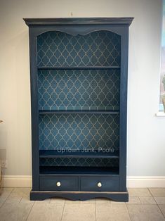 a blue bookcase with an ornate pattern on the top and bottom shelf, in front of a white wall