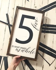 a hand holding up a framed sign with the number five on it that reads 5 is what makes a whole hole