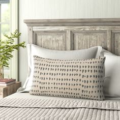 a bed with white sheets and pillows in front of a wooden headboard next to a potted plant