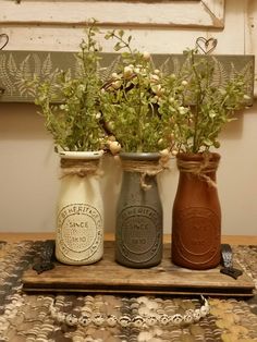 three jars with flowers in them sitting on a table next to a wall hanging frame