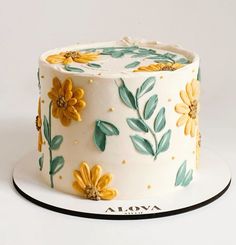 a white cake with yellow flowers and leaves on it's side, sitting on a plate