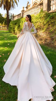 a woman in a long white dress standing on grass with her back to the camera