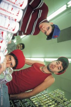 three men are standing in a room with stacks of beer bottles and cans on the floor