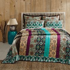 a bed covered in a multi colored comforter and pillows next to a wooden wall