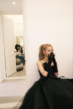 a woman in a black dress sitting on the floor with her hand up to her face