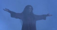 a person with long hair standing in front of a foggy sky and holding their arms out