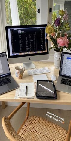 two laptops and a desktop computer sitting on a wooden desk in front of a window