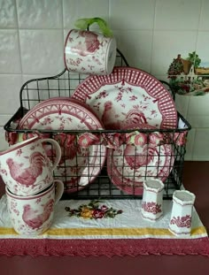 red and white dishes are stacked in a wire basket on a countertop next to cups and saucers