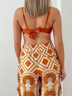 The Blair Sleeveless Tie Back Top his giving off sunny weather vacay vibes all day! This top has adjustable spaghetti straps and a tie back for ease of wear and a shiny mimosa colored fabric that pairs perfectly with the Hawaiian Sunset Kimono and the Hawaiian Sunset Wide Leg Pant for a flirty fun day into night look. Model is 5'10" wearing a size Medium 82% Nylon - 18% Spandex Hand Wash Cold - Do Not Bleach - Hang to Dry Chic Beach Bottoms With Built-in Bra, Vacation Halter Cami Top With Built-in Bra, Summer Poolside Halter Top With Spaghetti Straps, Summer Bandeau Halter Top With Tie Back, Summer Bandeau Tank Top With Straps, Strappy Tank Top For Beach Vacation, Vacation Tank Top With Straps For Beach Season, Vacation Beach Season Tank Top With Straps, Summer Beach Tank Top With Built-in Bra