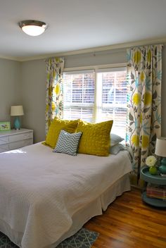 a white bed sitting in a bedroom next to a window with yellow and blue pillows