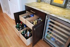 an open drawer in the middle of a kitchen with wine bottles and other condiments