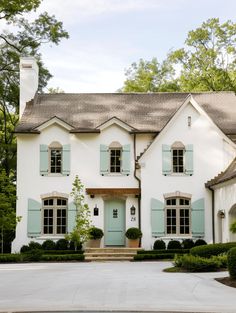 a large white house with blue shutters on the front and side windows, surrounded by greenery