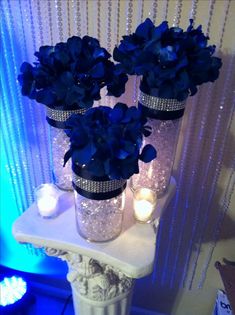 three vases filled with blue flowers sitting on top of a white table next to candles