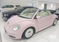 a pink convertible car is on display in a showroom with other cars behind it