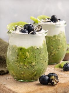 two jars filled with blueberries and kiwis on top of a cutting board