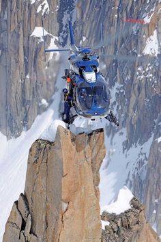 a helicopter is flying over a mountain with snow on the ground and mountains in the background