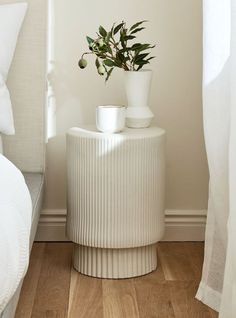 a white vase with a plant in it next to a bed