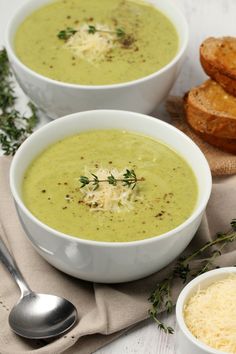 two white bowls filled with soup next to some bread and parmesan cheeses