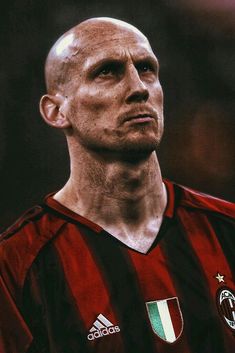 a man with a bald head wearing a red and black striped soccer jersey looking off to the side