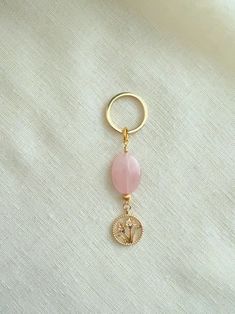 a gold key chain with a pink bead hanging from it's end on a white cloth