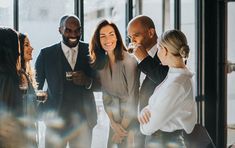 a group of people standing around each other smiling and having drinks in front of them