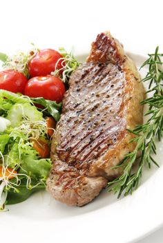 a white plate topped with meat, salad and tomatoes