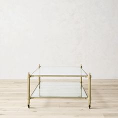 a glass and brass coffee table sitting on top of a hard wood floor in front of a white wall