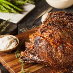 a large piece of meat sitting on top of a wooden cutting board next to some vegetables