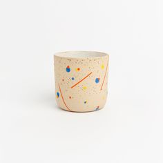 a white cup with orange and blue splatkles on the outside, sitting against a white background