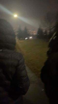 two people walking down a path at night with the lights on in the foggy sky